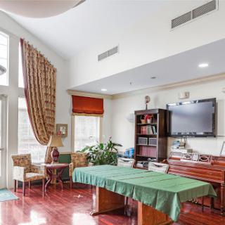 A well-lit living room with a green table, cozy seating, and a television.