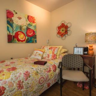 A cozy bedroom with floral-themed decor, featuring a comfortable bed, a chair, and colorful wall art.
