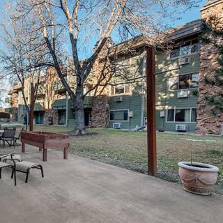 A view of an apartment building with a spacious patio area featuring chairs and trees.