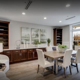 A modern dining room with a wooden table, white chairs, and built-in bookshelves.
