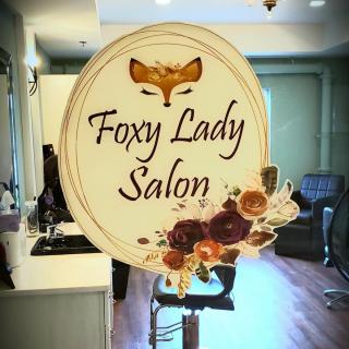 A stylish sign for 'Foxy Lady Salon' featuring a fox logo and floral decorations, displayed inside the salon.
