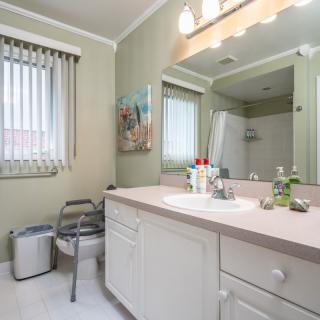 A well-lit bathroom featuring a spacious vanity, mirror, and natural light from the window with blinds.