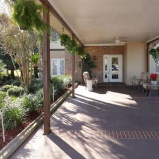 A shaded porch with outdoor furniture and lush greenery.
