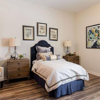 A cozy bedroom with a single bed, complemented by nightstands, lamps, and framed artwork on the walls.