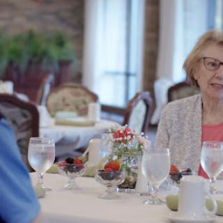 An elderly woman enjoying a conversation over lunch in a cozy restaurant setting.