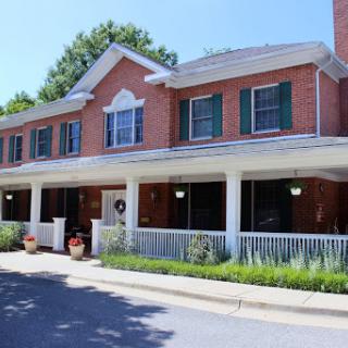 A charming two-story brick building featuring green shutters and a welcoming porch.