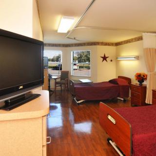 A hospital room with two beds, a television, and seating area by the window.
