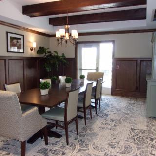 A well-appointed dining room featuring a rectangular table, upholstered chairs, wooden ceiling beams, and decorative plants.