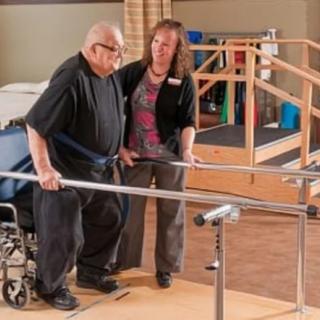 An elderly man receiving assistance during a physical therapy session with the help of parallel bars.
