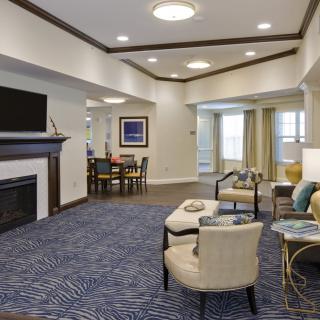 A spacious living room with a fireplace and modern furnishings, featuring a cozy seating area and a dining table in the background.