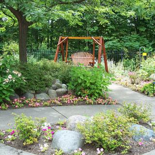 A tranquil garden with a wooden swing surrounded by lush greenery and a winding pathway.