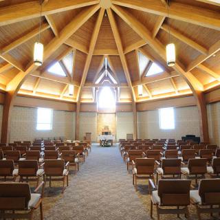 A spacious church interior with wooden beams and arranged seating facing the altar.