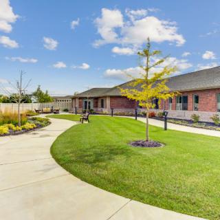 A well-maintained garden with a winding pathway leading to a modern building, set under a partly cloudy sky.