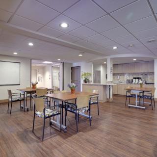 A modern interior space featuring several tables and chairs, illuminated by overhead lighting with a wooden floor setting.