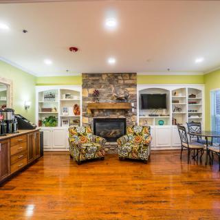 A cozy living room with a stone fireplace, built-in shelves, and vibrant chairs on hardwood flooring.