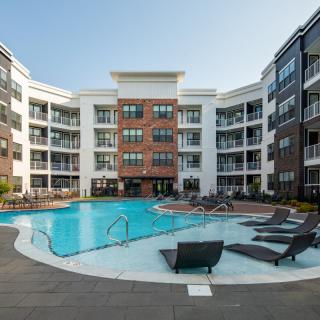 A modern apartment complex featuring a spacious swimming pool in the central courtyard.