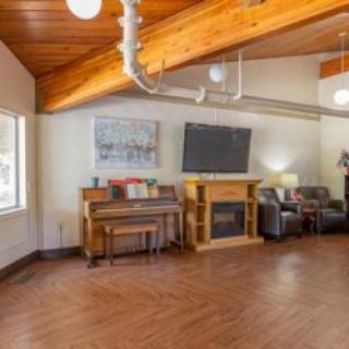 A cozy living room featuring a wooden ceiling, piano, fireplace with a TV above, and comfortable seating.