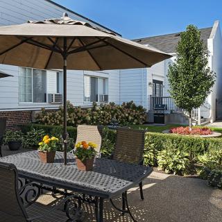 A cozy outdoor patio with a table, chairs, and an umbrella surrounded by a well-maintained garden.