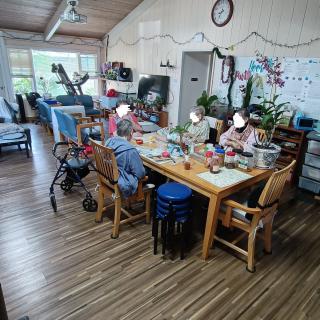 A group of elderly individuals engaged in a crafting activity around a table in a cozy room.
