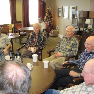 A group of seniors seated around a table having a discussion and enjoying coffee.