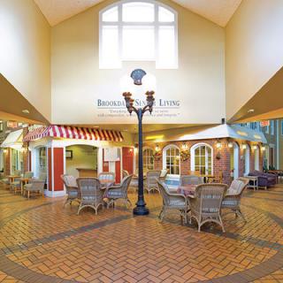 A spacious indoor atrium with a brick floor, featuring a central street lamp, tables, and chairs for seating.