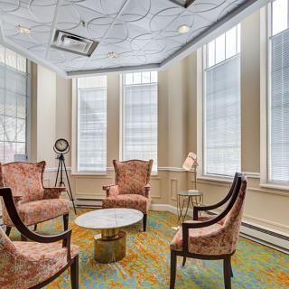 A cozy sitting area with elegant chairs and a round table, illuminated by natural light from large windows.