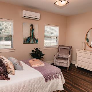 A cozy bedroom with modern decor, featuring a bed, armchair, and dresser under warm lighting.