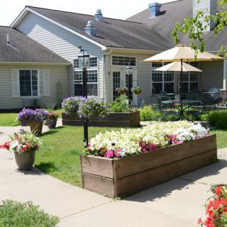 A beautifully landscaped garden with flower-filled raised beds and potted plants, adjacent to a patio area with an umbrella.