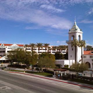 A scenic view of a charming building with a tower, surrounded by palm trees and a clear sky.