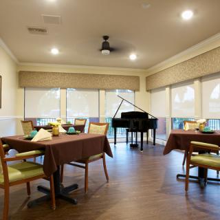 A cozy dining area with tables, chairs, and a grand piano in the corner.