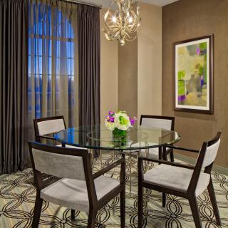 A stylish dining room with a glass table and elegant chairs, featuring a modern chandelier and artwork on the wall.