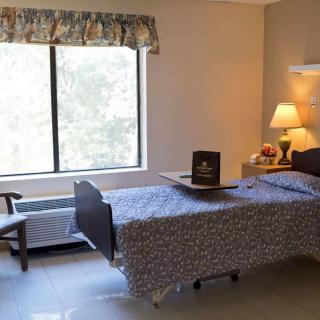 A hospital room featuring a bed, nightstand, and window with curtains.