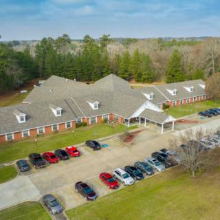 Aerial view of a large building with a parking lot surrounded by greenery.