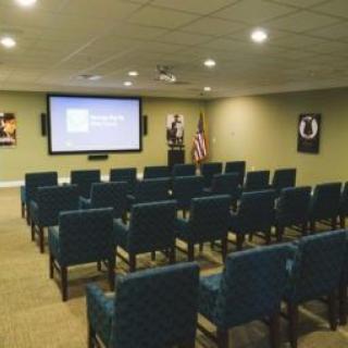 An empty theater room with rows of chairs facing a presentation screen.
