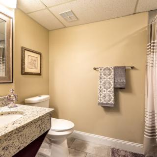 A clean and modern bathroom with beige walls, featuring a sink, mirror, toilet, and towel rack next to a shower curtain.