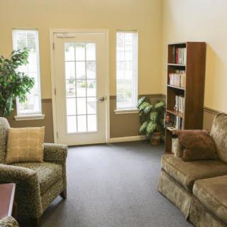 Cozy living room with a sofa, armchair, bookshelf, and natural light from windows.