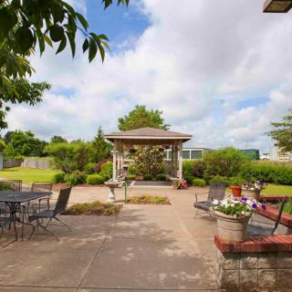 A peaceful garden patio featuring a gazebo, surrounded by lush greenery and outdoor seating under a cloudy sky.