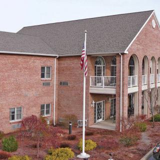 A two-story brick office building with a flagpole displaying the American flag in front of landscaped grounds.