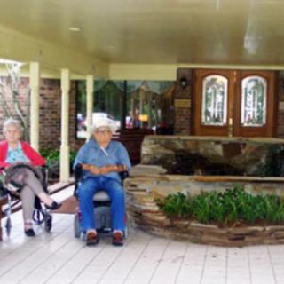 Two elderly people relaxing on a porch, one in a wheelchair.