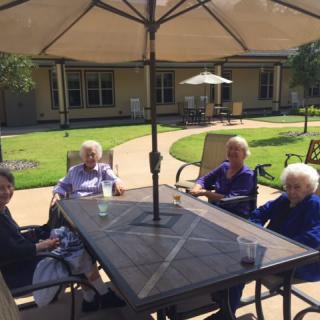 A group of seniors sitting together under a patio umbrella on a sunny day.