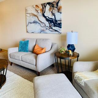 A cozy living room with a modern sofa and armchair, accented by colorful cushions and abstract artwork.