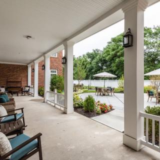 A covered porch with outdoor seating overlooking a garden and patio area.