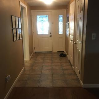 A well-lit hallway leading to a front door with tiled flooring.
