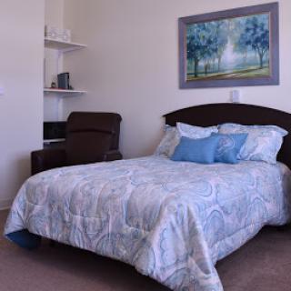 A cozy bedroom featuring a neatly made bed with decorative pillows and a framed painting on the wall.
