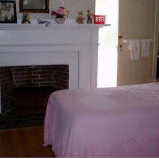 A cozy bedroom featuring a fireplace and a bed with a pink bedspread.