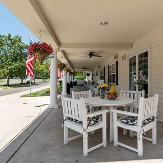 A cozy outdoor patio with white furniture, adorned with flowers and American flags, offering a serene spot for relaxation.