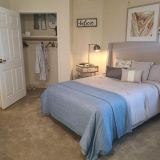 A cozy and neatly arranged bedroom with a bed, side table, lamp, and open closet.