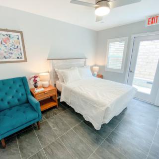 A bright and modern bedroom with a white bed, blue chair, nightstands, and artwork on the wall.