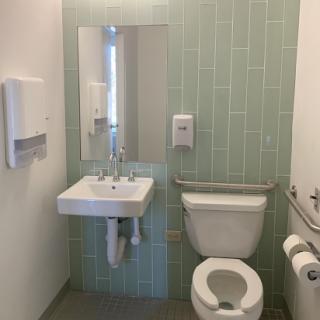 A modern and clean restroom featuring green tiled walls, a sink with a mirror, and accessible facilities.