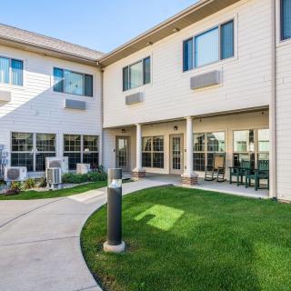 A modern residential building with a landscaped courtyard area, featuring grass and outdoor seating under clear skies.